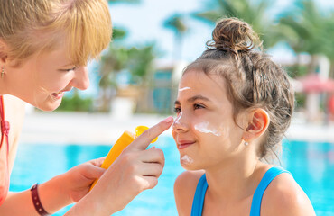 The child is smearing sunscreen on the mother. Selective focus.