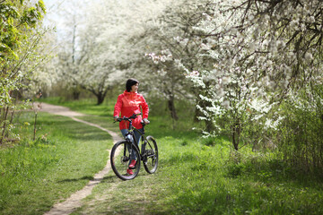 Obraz premium Beautiful woman on a bike in a blooming spring garden. Beautiful mature woman posing for the camera in a blooming spring garden.