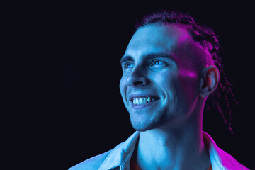 Caucasian young man's portrait on dark studio background in neon. Concept of human emotions, facial...