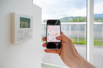 Hand holding a mobile phone showing an home automation app to manage online technology in a modern loft. - 432174612