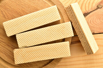 Several sweet vanilla waffles on a round wooden tray, close-up, on a wooden table, top view.