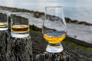 Tasting of dram single malt scotch whisky on seashore in Scotland, old wooden pole with whisky glass