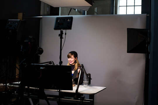 Smiling female entrepreneur explaining about product while broadcasting through television camera at office