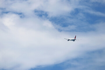 Airplane flying in the blue sky on background of white clouds, rear view. Twin-engine commercial plane during the turn, turbulence and travel concept