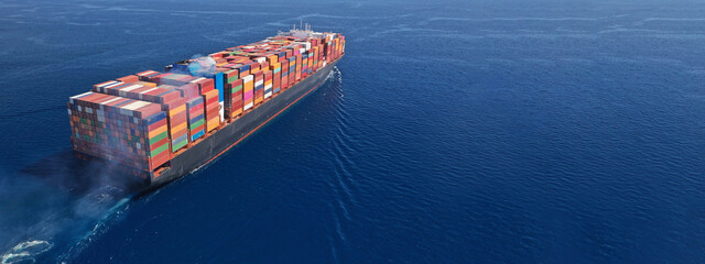 Aerial drone ultra wide photo above huge colourful container carrier vessel cruising deep blue open...