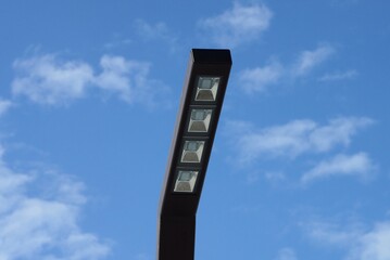  one brown metal pole with a row of white LED bulbs against a background of blue sky and gray cloud