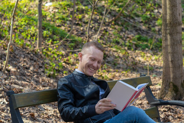 Fototapeta premium a smiling man reads a book on a park bench