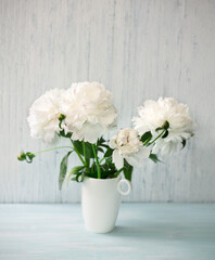 Garden white peonies  in a white porcelain vase  on a light blue wooden background, close up