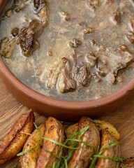 Pot of rich meat soup with pork or lamb on wooden table with baked potatoes in foreground. Hearty and fatty broth. High angle view. Close up shot.