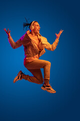 Caucasian young man in headphones isolated on blue studio background in neon. Concept of human emotions, facial expression.