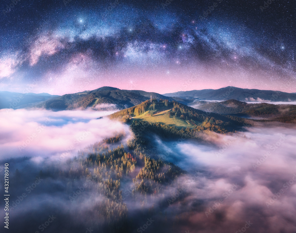 Wall mural milky way arch and mountains in low clouds at starry night in summer. landscape with pink sky with s