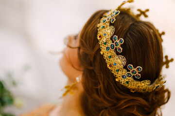 A woman with a beautiful hairstyle in a gold crown with stones, close-up. Bride wearing a crown on...