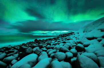 Obraz premium Northern lights. Aurora borealis over ocean in Teriberka, Russia. Starry sky with polar lights and clouds. Night winter landscape with bright aurora, stars, sea, snowy stones in blurred water. Travel