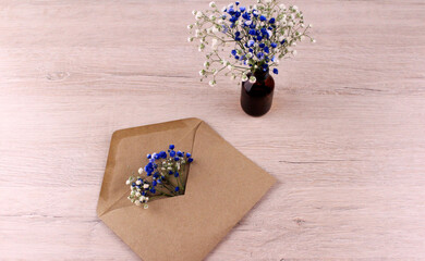 Paper envelope with gypsophila flowers and glass bottle with flowers on wooden table