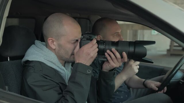 Two men sitting in a car and taking a picture with a professional camera, a private detective or a paparazzi spy.