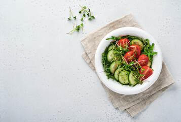 Fresh salad with tomato, cucumber, vegetables, microgreen radishes in white plate on grey stone background. View from above. Concept vegan and healthy eating.