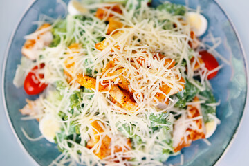 Meal of salad caesar on table. Dish with tomatoes, herbs, chicken and egg sprinkled with cheese. Concept of menu in cafe or restaurant.