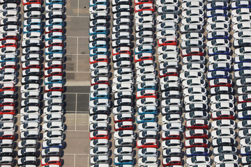 An aerial view taken from a helicopter of a huge car import storage area. Many rows of new vehicles of different colours waiting at a port in Britain. An abstract striped pattern.