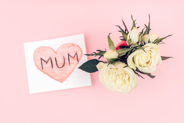 A gift from a child for mothers day - a hand made card with white rose flowers on pink background. Flat lay, top view.
