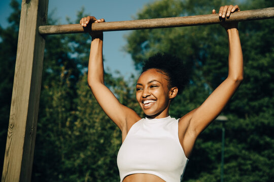 Smiling sportswoman hanging on monkey bar in park during sunny day