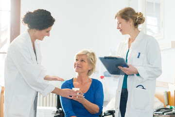 Obraz premium nurse passing drink to mature lady in wheelchair