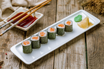 salmon roll maki on white plate with ginger and wasabi on old wooden table