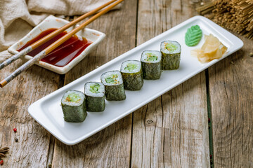 roll with cucumber maki on white plate with ginger and wasabi on old wooden table