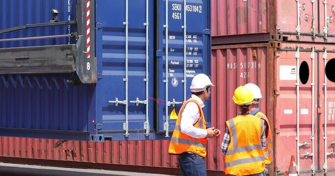 Hispanic man harbor worker talking on the walkie-talkie radio and control loading containers at container warehouse. container yard port of import and export goods