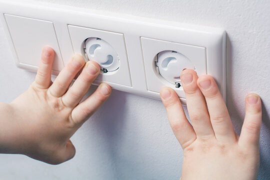 Two Child Hands Touching A Wall Socket With Safety Plugs - Prevent Child Hazard Concept