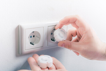 Hand Inserting Baby Safety Plugs Into Wall Socket To Prevent Danger At Home