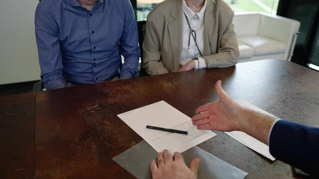 Banker hands over a contract to his clients to sign it. He tries to convince the young insecure couple by gesticulating with his hands