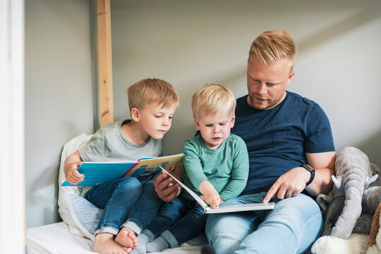 Father reading book while sitting with children in bedroom