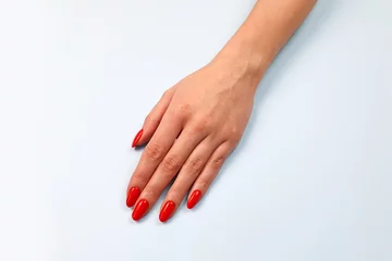 Caucasian young woman's hand with red nails on light blue table. Top view, copy space.