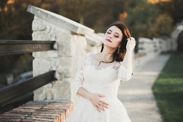 Beautiful bride in elegant white dress holding bouquet posing in park
