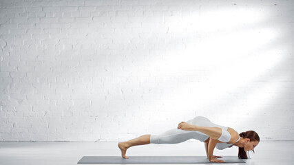 Young woman practicing yoga near white wall at home.