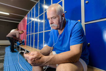 Fototapeta na wymiar senior man listening to earphones in locker room