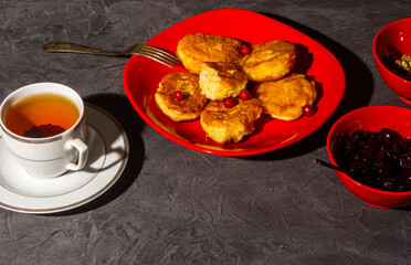 Homemade dish - fried pancakes with jam in a red bowl, a cup of black tea, and walnuts, simple rustic food, black background, close-up.