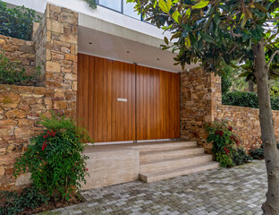Fototapeta premium elegant house front huge entrance wooden door and stone fence with green plants, Athens Greece