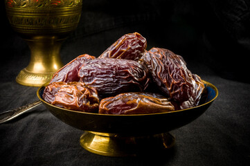 Big luxury dried date fruit in bowls on the dark surface, kurma ramadan kareem concept, close up.