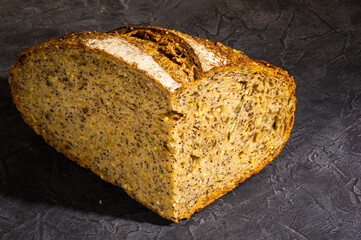 Slice of rustic natural yeast-free bread with flax, poppy seeds, sesame seeds, millet, pumpkin and sunflower seeds, on a black background, hard light, photo in a low key.