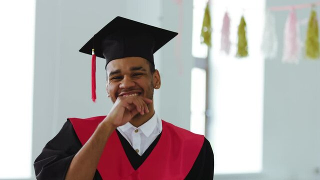 a student wearing square caps and a black and red gown in front of the screen during the broadcast of the graduation ceremony. Insert in to zoom or chat program