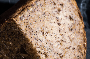 Slice of rustic natural yeast-free bread with flax, poppy seeds, sesame seeds, millet, pumpkin and sunflower seeds, on a black background, hard light, photo in a low key, close up.