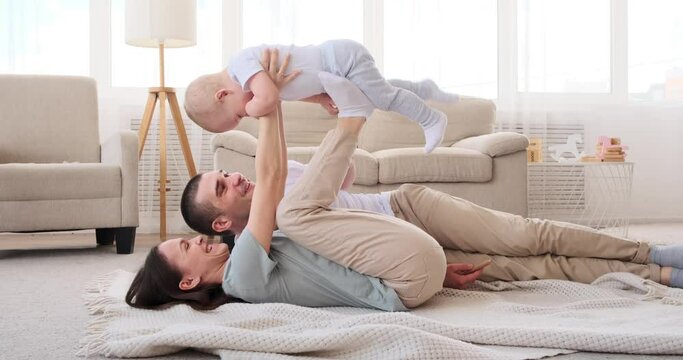 Parents having fun playing with baby son lying on carpet at home