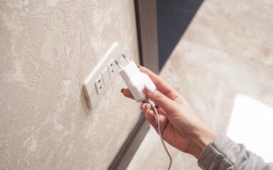 Woman plugs the phone charger into the socket.