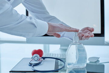 The doctor is in his office on the premises of the clinic. Disinfects hands with a dispenser