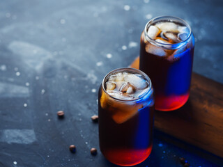 Two stylish glasses of cold brew coffee. Colored blue light. On a wooden board , black background