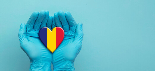 Doctors hands wearing surgical gloves holding Romania flag heart
