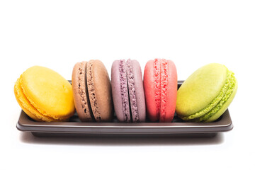 Pastel colorful many macarons with different flavors on plastic tray isolated on white background. Macaron is a delicate meringue-based cookie sandwich It is a dessert of French origin.