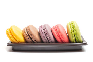 Pastel colorful many macarons with different flavors on plastic tray isolated on white background. Macaron is a delicate meringue-based cookie sandwich It is a dessert of French origin.