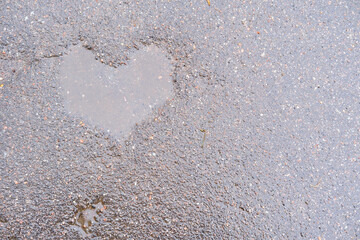pavement after rain with a puddle in a shape of heart. wet dark grey road with flaws in a form of a heart filled with water, space for text, seeing love everywhere, natural imperfection of roads